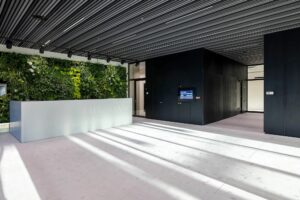 Moderne ontvangsthal van The Joan aan de Joan Muyskenweg met een groene plantenwand en een strak baliedesign.